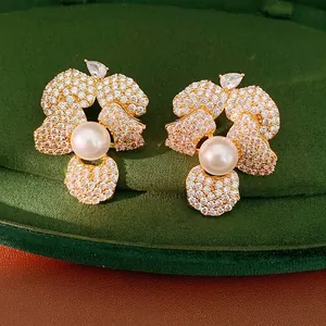 Elegant flower-shaped stud earrings with sparkling zircons and pearls on green velvet.