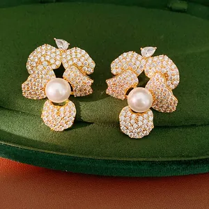 Macro detail of elegant zircon flower stud earrings with a central pearl on green velvet