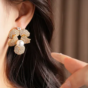 Close-up view of elegant gold flower earrings with CZ stones and a central pearl.