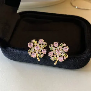 Close-up of sparkling zircon flower earrings with pink and green stones on black box