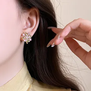 Detailed view of gold flower stud earrings featuring pink and white cubic zirconia stones