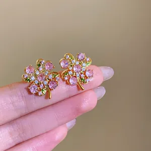 Detail view of sparkling zircon flower earrings with pink and green stones on a finger