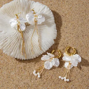 Close-up detail of white acrylic flower petal earrings with gold tassels on sandy beach