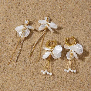 Elegant gold tassel earrings with white acrylic petals and pearls on a sand background.
