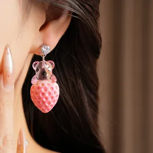 Gros plan d'une boucle d'oreille en résine avec ours rose et fraise, dotée d'un clou en zircon.
