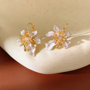 Elegant flower huggie earrings with zircon and white enamel on a ceramic tray.