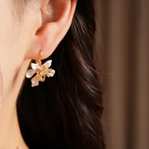 Close-up of elegant gold flower drop earrings with white enamel and zircon stones.