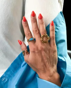 Close-up detail of geometric 18K gold plated rings on fingers with vibrant red nails.