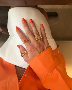 Detail shot of three gold geometric open rings on a hand with vibrant orange nails