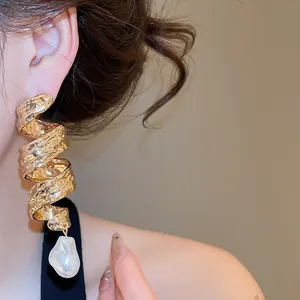 Vue détaillée de boucles d'oreilles torsadées dorées avec goutte de perle baroque.