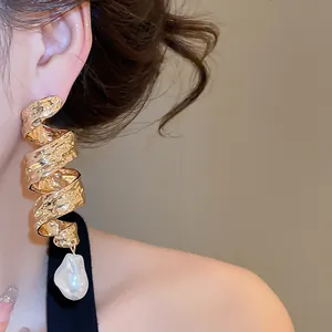 Gros plan de boucles d'oreilles torsadées en or avec perle baroque sur un modèle.