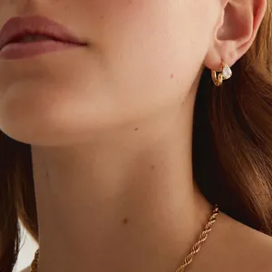 Close-up of gold hoop earring with pear-shaped stone and matching rope chain necklace.