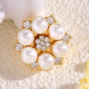 Vista detallada de un elegante broche de flor con perlas, cristales y base dorada