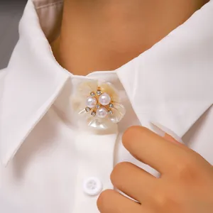 Vista detallada de un broche decorativo de flor de perlas en el cuello de una camisa.