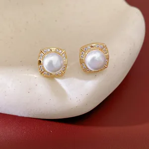 Detailed close-up of gold-plated square stud earrings with central pearls and zircon halo