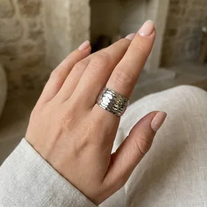 Gros plan d'une bague large martelée minimaliste en finition argentée portée au doigt