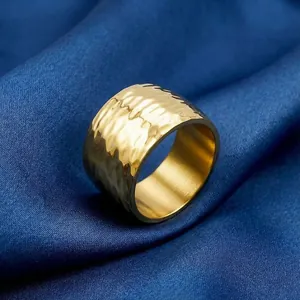 Close-up of a wide golden stainless steel ring with a hammered texture on blue fabric.