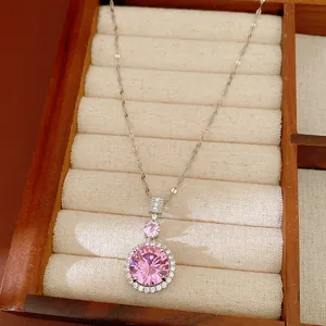 Détail d'un pendentif en zircone rose sur une chaîne argentée dans une boîte en bois.
