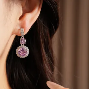 Vue détaillée de boucles d'oreilles pendantes en zircon rose avec halo rond portées à l'oreille