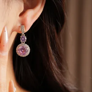 Détail de boucles d'oreilles pendantes en zircon rose avec design halo sur l'oreille.