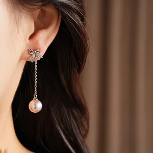 Gros plan d'une boucle d'oreille nœud argentée avec une perle rose pendante sur l'oreille