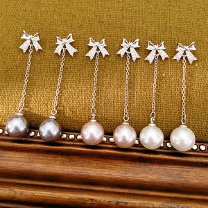 Gros plan de boucles d'oreilles nœud et perle avec zircons brillants en trois couleurs.