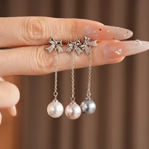 Détail de boucles d'oreilles nœud et perle en trois couleurs : blanc, rose et gris.