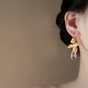 Dettaglio di orecchini a foglia d'oro e fiori con perle e goccia di cristallo su modella