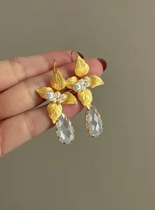 Dettaglio di eleganti orecchini a foglia d'oro con perle e gocce di cristallo puro.