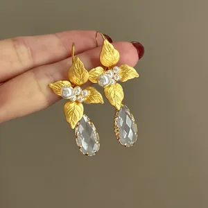 Primo piano di orecchini a fiore dorati con perle e gocce di cristallo sfaccettato