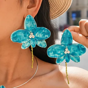 Close-up of blue enamel orchid earrings with rhinestones and gold stem detail