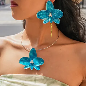 Detailed shot of large blue enamel flower necklace and matching earring on model