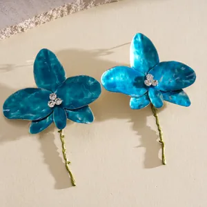 Close-up of dainty blue enameled flower earrings with rhinestone centers and long stems.