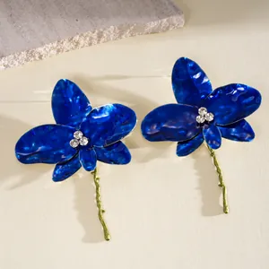 Detailed view of blue enamel orchid flower earrings with sparkling rhinestone centers and gold stems