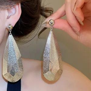 Détail de boucles d'oreilles pendantes argentées texturées portées par un modèle