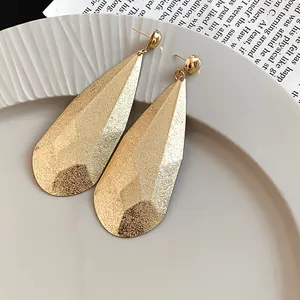 Gros plan montrant la texture froissée des boucles d'oreilles goutte d'or