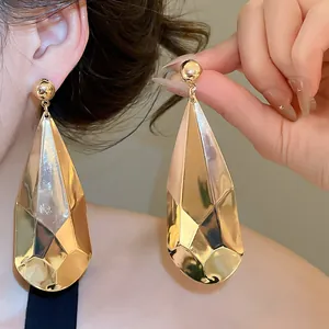 Détail de boucles d'oreilles pendantes dorées à facettes en forme de goutte