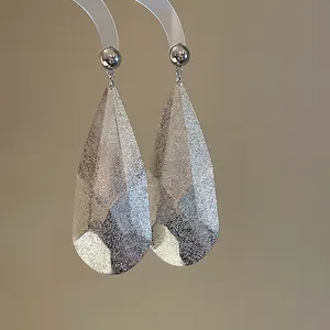 Gros plan montrant la surface argentée texturée unique de ces boucles d'oreilles goutte.