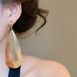 Gros plan détaillé d'une grande boucle d'oreille goutte en métal doré à surface facettée.