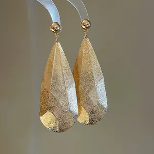 Vue macro de boucles d'oreilles goutte d'eau dorées avec finition texturée