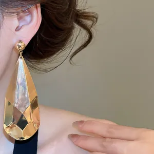 Détail de boucles d'oreilles goutte d'eau dorées avec un design plissé et facetté