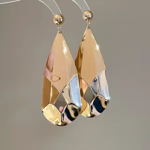 Gros plan de boucles d'oreilles gouttes facettées dorées avec une finition géométrique