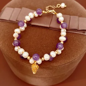 Close-up detail of freshwater pearl and amethyst beaded bracelet with gold pinecone charm.