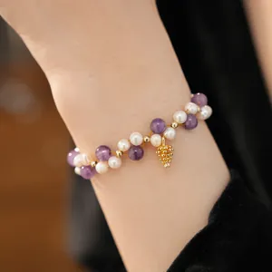 Close-up of 18k gold plated freshwater pearl bracelet with amethyst beads and pinecone charm