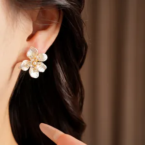 Close-up of white enamel flower stud earrings with pearls and zircons on a model's ear.