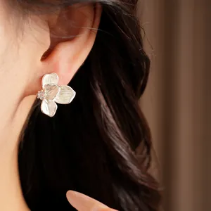 Close-up view of a white enamel flower stud earring with a sparkling zircon center