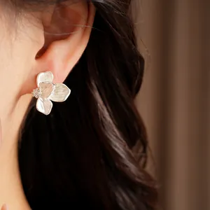 Detail close-up of white enamel flower stud earring with zircon center worn on ear