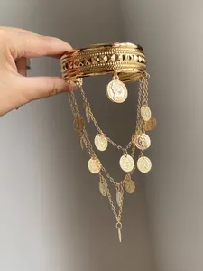Détail d'un bracelet de bras doré avec breloques pièces et chaînes métalliques.