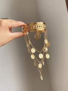 Vue détaillée d'un large bracelet doré avec des glands en pièces de monnaie à la main.