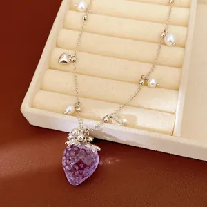 Gros plan détaillé du pendentif fraise en résine violette et collier de perles fines.